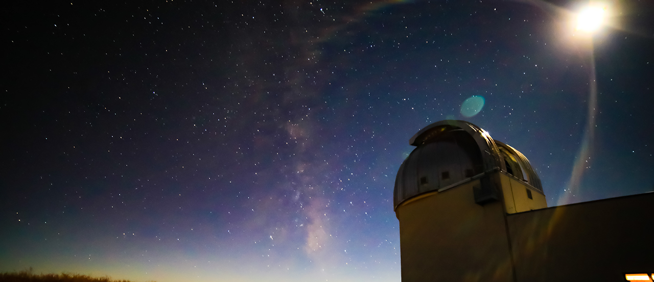 Image of the Magdalena Ridge Observatory telescope at sunset. The exterior view is from the ground looking towards the telescope, with stars in the background.